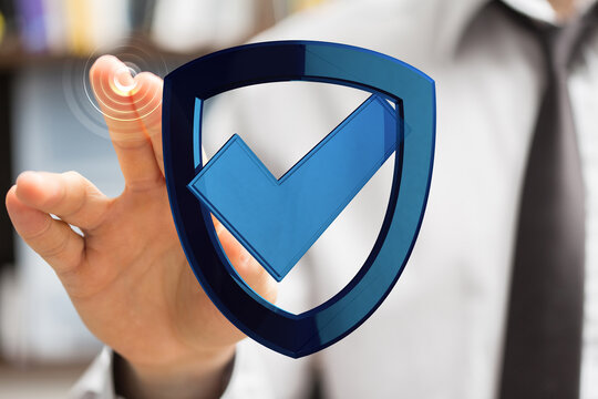 A business person's hand touches a digital shield icon with a check mark, representing concepts like data protection and cyber securi