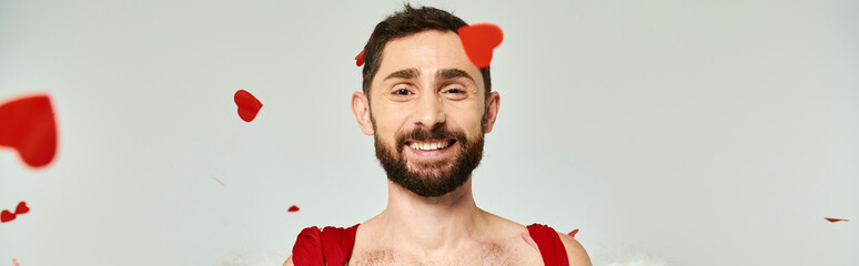 funny cupid man smiling at camera under red heart-shaped confetti, st valentines party, banner