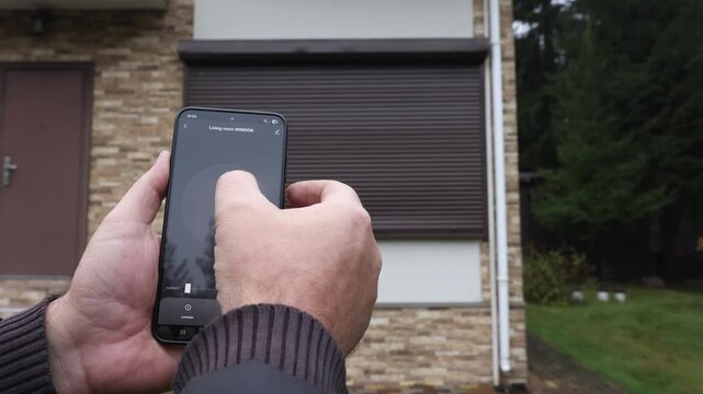 User's hands open Rolling Shutter Window using smart home mobile app. High quality 4k footage