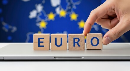 Euro currency concept with wooden blocks spelling EURO hand placing the last block with the European Union flag in the background