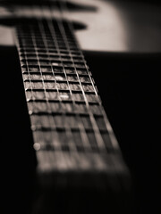 Black and white guitar with faint sepia, light hitting central part in focus, edges dark, neck extending into frame, background guitar softly blurred, moody and atmospheric composition emphasizing