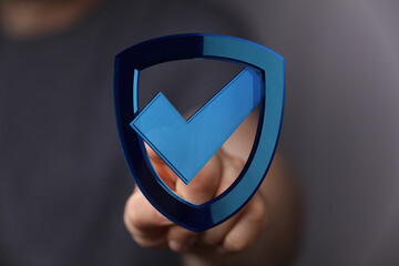 Close-up of a hand holding a blue shield with a checkmark, representing security, protection, and...