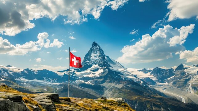 A scenic view of the Matterhorn mountain in Switzerland, with a Swiss flag waving in the foreground. The sky is blue with fluffy clouds.