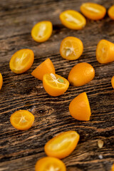 lots of ripe orange kumquat cut on a wooden table, a group of scattered and sliced kumquat fruits on a wooden table and board