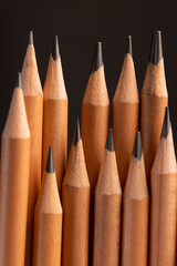 a group of wooden pencils with a black lead on a black background, stacked pencils made of wood and a lead made of graphite