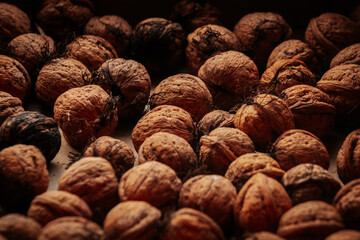 A rustic arrangement of whole walnuts scattered on a brown paper surface reveals natural textures and earthy tones. Soft lighting creates a warm, organic feel.
