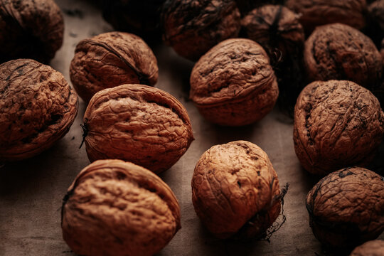 A rustic arrangement of whole walnuts scattered on a brown paper surface reveals natural textures and earthy tones. Soft lighting creates a warm, organic feel.