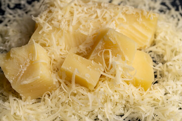 grated yellow hard cheese on a grater for pizza or pasta, yellow grated cheese with pieces for cooking various foods