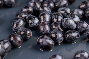 a ripe blue grape, torn from a branch, lying on a bowl, covered with drops of water, wet fruits of pure blue grapes on a blue bowl during cooking
