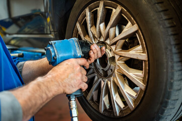 Mechanic repairing car wheel using impact wrench in workshop