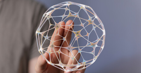 Close-up of a hand holding a glowing 3D-rendered abstract structure. The image evokes concepts of technology, networks, connection, a