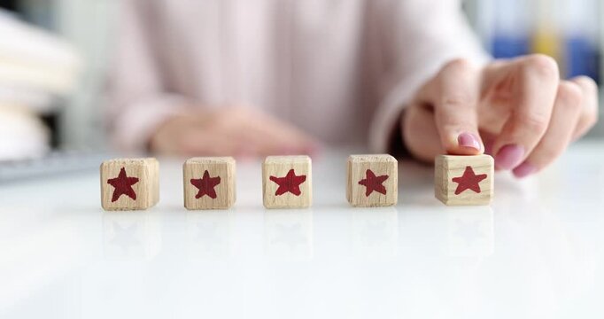 Woman hand arranges four star blocks on table and smiles. Hand places fifth cube and completes rating row showing perfect service score