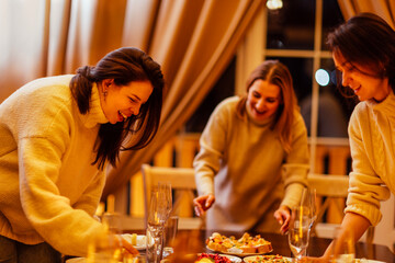 Young women are preparing a Christmas lunch. Friends chat and set the festive table. Girls are eating and having fun at a New Year Eve party.