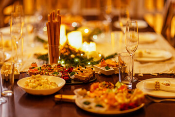 Close-up of delicious snacks on a festive table. Candles and Christmas decorations. Plates and glasses. Tasty dishes for a celebratory lunch.