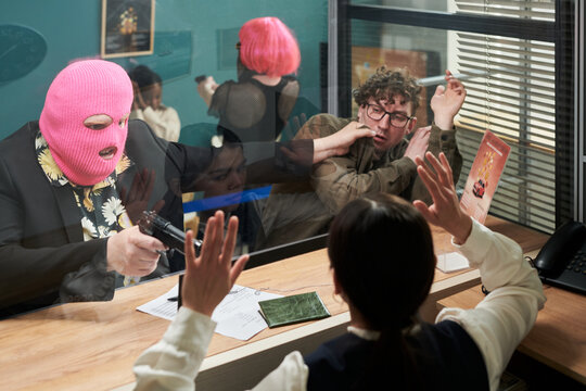Caucasian man wearing pink ski mask pointing handgun at young adult Caucasian man and young adult teller during bank robbery, victims raising hands in fear