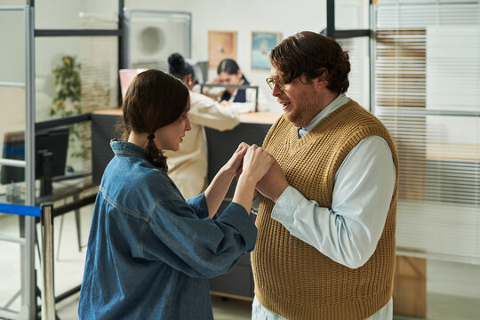 Caucasian young adult woman holding hands and talking with man in bank office setting, two women in background, glass partitions visible