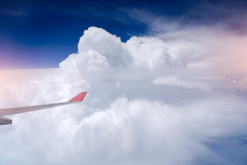 Stunning view from airplane window of a wing above scattered cumulus cloud layer and mountainous landscape. Traveling by aeroplane high above a clear blue sky.