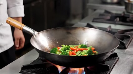 A chef stir-fries fresh vegetables in a hot wok over a gas burner in a professional kitchen. - Powered by Adobe