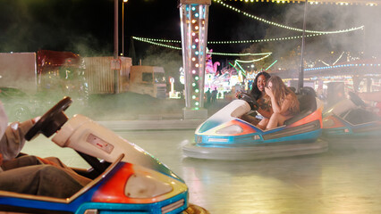 Two young women enjoying a thrilling ride on bumper cars at a lively night fair