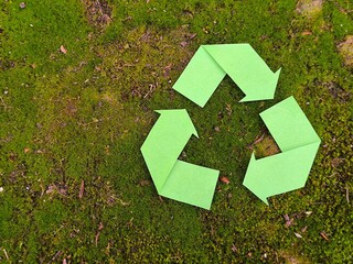 green recycling symbol made of paper on a green moss background