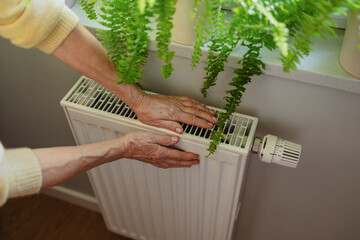 Senior woman warming her hands on a radiator at home, close-up
