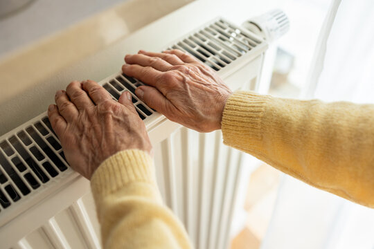 Senior woman warming her hands on a radiator at home, close-up
