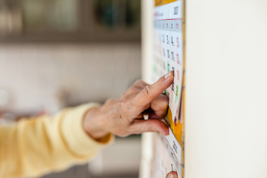 Senior woman using a wall calendar in her kitchen, focus on finger