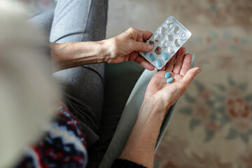 Senior woman taking her medication at home, close-up of hands
