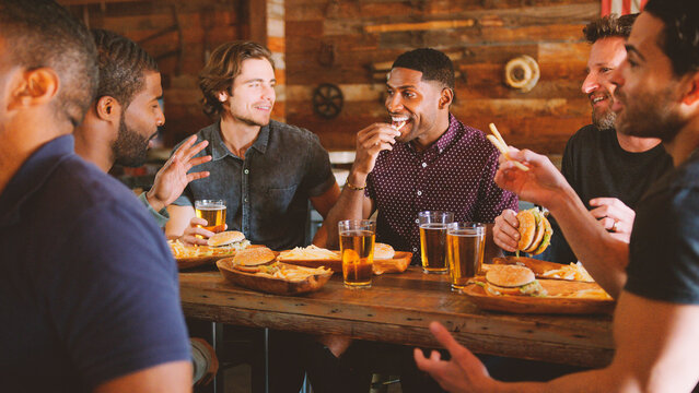 Male Friends Drinking Beer And Eating Burgers In Sports Bar
