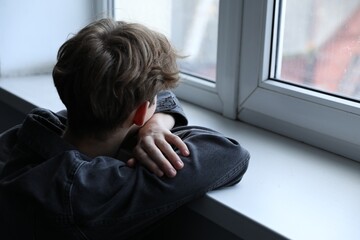 Depressed teenage boy near window at home, space for text © New Africa
