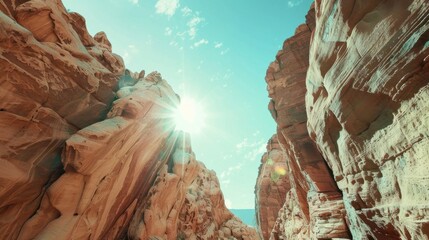 A stunning view of a narrow canyon with towering red rock formations under a bright blue sky. Sunlight beams through the rocky crevices, creating a dramatic effect.