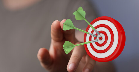 Close up of a hand holding a dart, hitting the target board. Symbol of success and accuracy,...