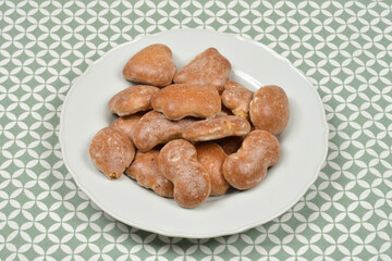 A small pile of unglazed, brown gingerbread cookies is served on a white plate centered on a green and white patterned tablecloth