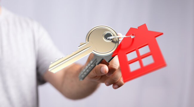 Hand holding keys with a house-shaped charm, representing homeownership, property investment, buying a new house. Suitable for real estate marke