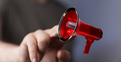 Close-up of a hand holding a red megaphone, symbolizing announcement, marketing, and communication...