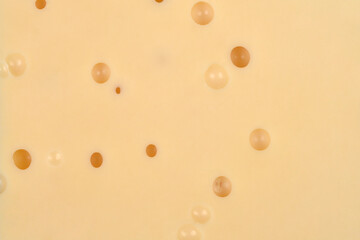 An extreme close-up of a block of Emmental or Swiss-style cheese, showing the smooth texture and...