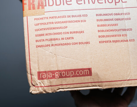 Paris, France - Dec 13, 2024: Close-up of a cardboard shipping box showing multilingual eco bubble envelope text and the visible Raja Group website logo, held by a hand against a neutral background.