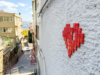 Istanbul, Turkey - August 29, 2025: Pixel style red mosaic love heart street art on a residential wall overlooking a narrow street and cityscape