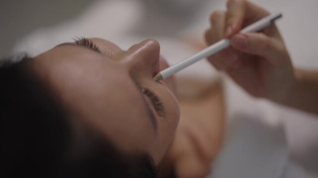 Close-up of professional plastic surgeon or cosmetologist using white pencil to mark lines on female patient face, preparing for cosmetic surgery or aesthetic treatment in modern aesthetic clinic.