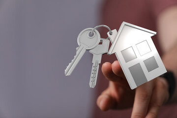 Close-up of a hand holding house keys and a house-shaped keychain, representing homeownership, real...