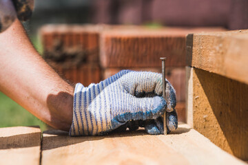A carpenter in cloth protective gloves nails wooden planks. Close-up of a nail hammered into a board.