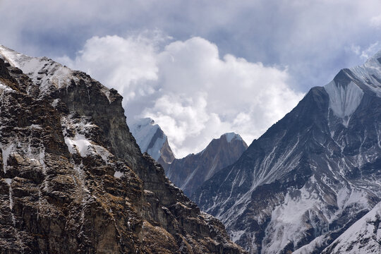 Views of the majestic Himalayas, Nepal, on the way to Annapurna Base Camp. Steep rocky mountains are partially covered in snow under a cloudy sky.