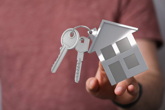 Person holding house keys and house shaped keychain, a symbol of home ownership, real estate, and new beginnings.
