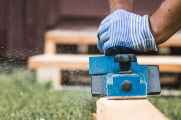 A man is whittling planks with an electric tool. A hand-held electric plane in the hands of a craftsman. Production of wood products. Construction, wood processing.