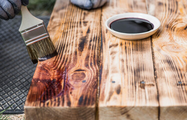 A worker applies a protective wood stain with a brush. The process of protecting and coating wooden boards. The process of restoring parquet flooring.