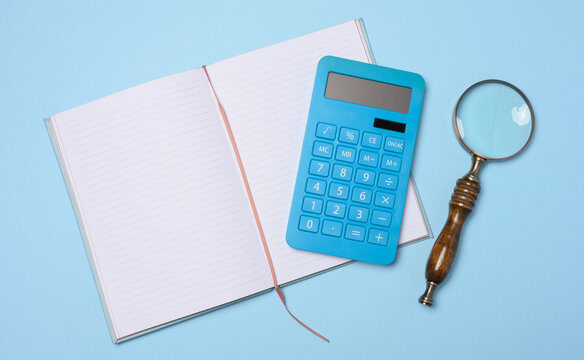 An open notebook, a blue calculator, and a vintage magnifying glass on a blue background.