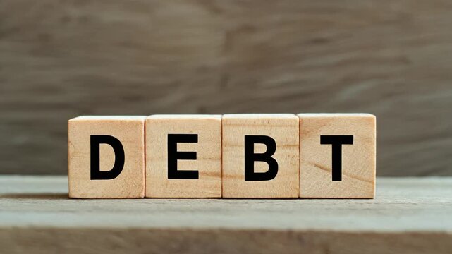The word DEBT spelled with wooden blocks on a wooden surface.