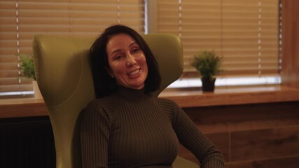 Portrait of cheerful female client seated in armchair in private therapy session, engaging with therapist, discussing mental health, challenges and progress in calm, confidential counseling room.
