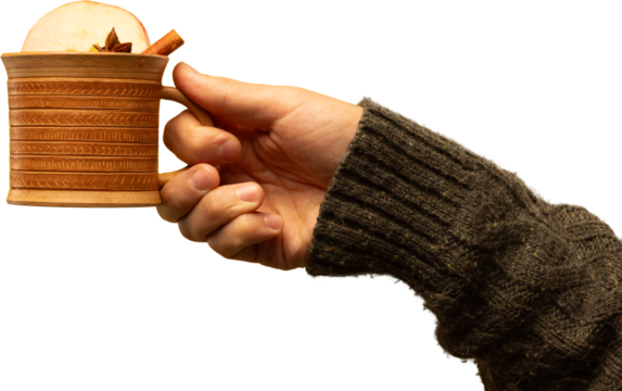 Hand holding clay mug with spiced warm drink and apple garnish on transparent background. Concept of rustic seasonal aesthetics, traditional flavors, food branding, and autumn-winter promo imagery.