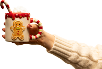 Hand holding gingerbread-themed holiday mug with candy cane and cream on transparent background. Concept of Christmas marketing, cozy lifestyle visuals, festive sweets, and warm emotional storytelling